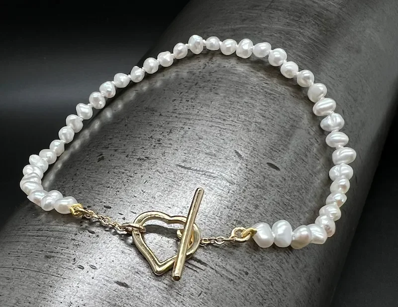 Perlenarmband mit goldener Herz- und Schlossschnalle auf dunklem Hintergrund.