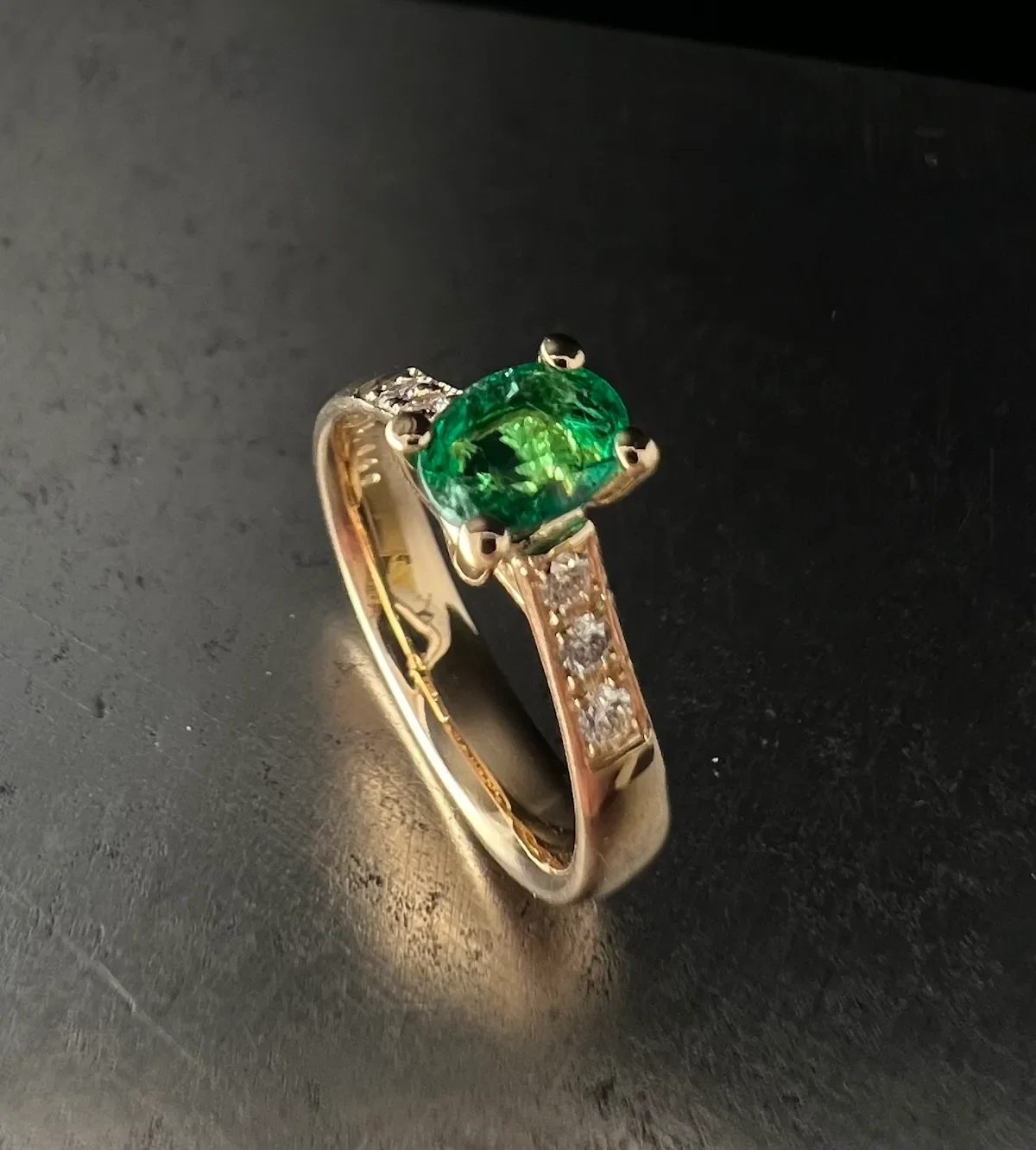 Verlobungsring aus Gelbgold mit ovalem Smaragd und Diamant-Pavé auf der Schiene, Isarschmiede München.