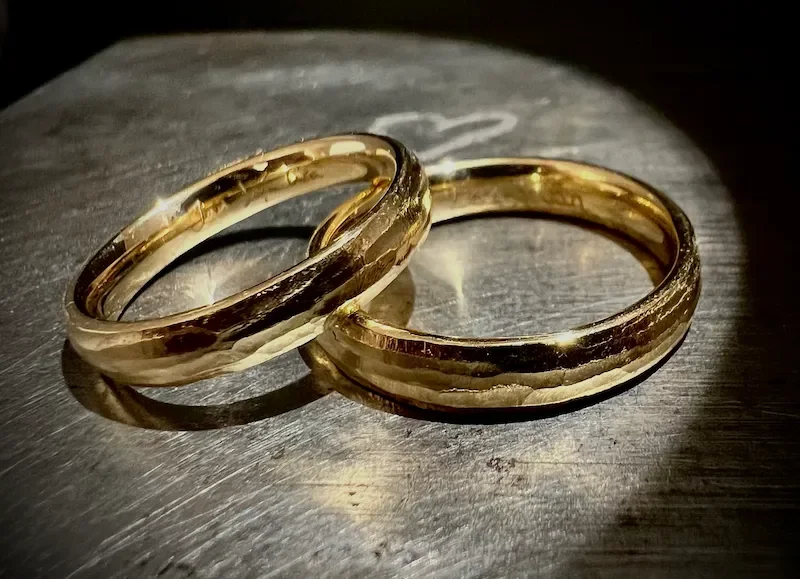 Zwei goldene Eheringe auf einer metallischen Oberfläche