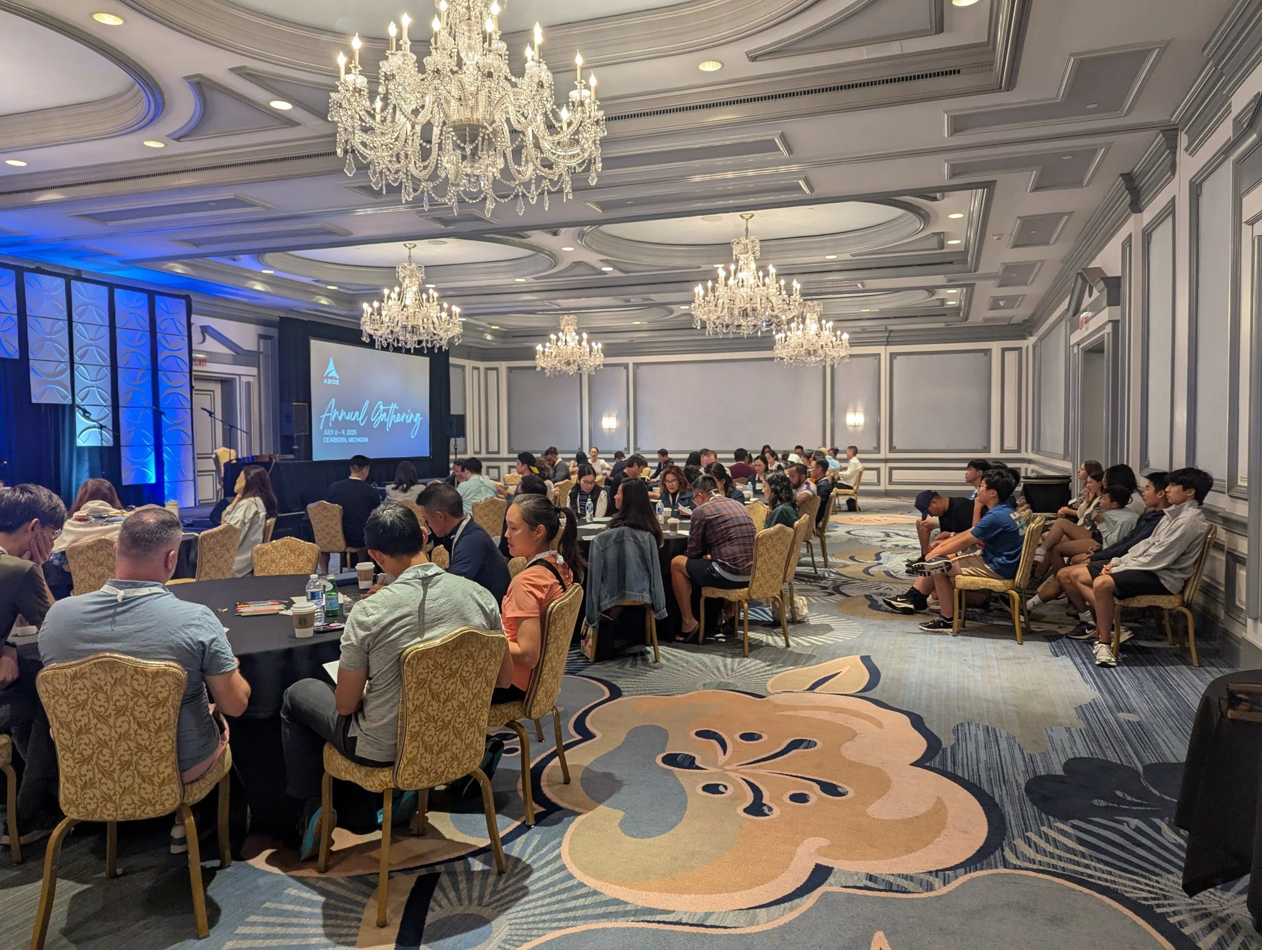 Adults and youth sitting in in a hotel ballroom during a conference session