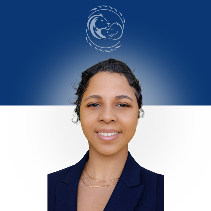 Smiling person with curly hair, wearing a light-colored collared shirt and necklace against a neutral background.