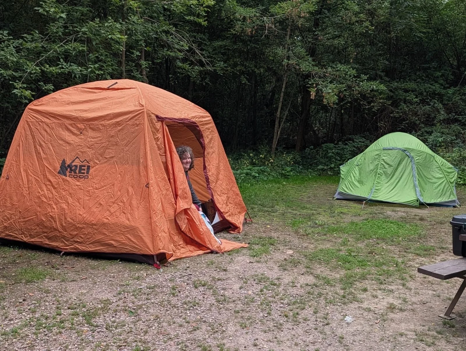 Naomi pokes her curly haired head out of her big orange tent. She has a very content smile on her face.