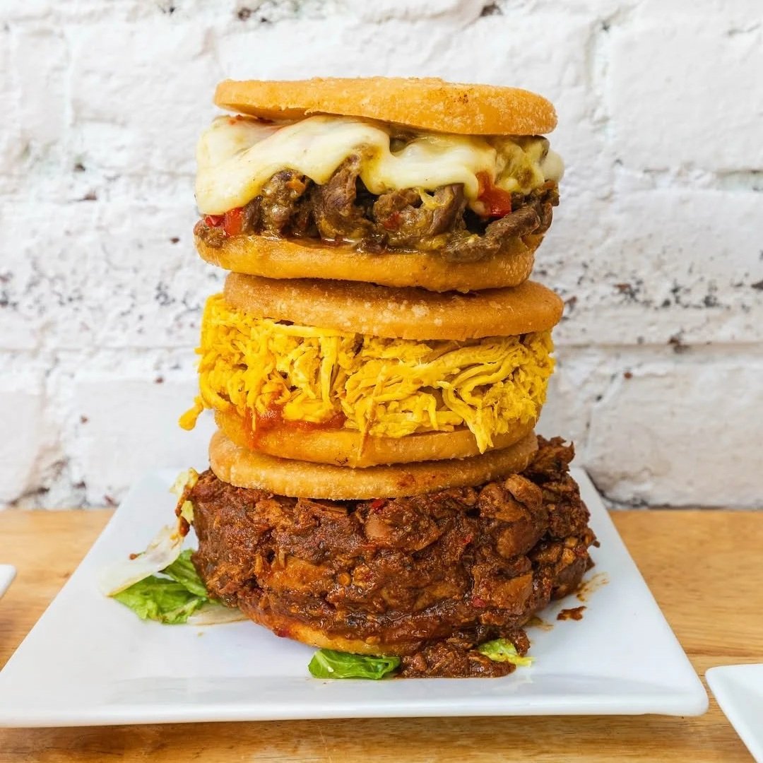 Stack of three stuffed arepas with meat, cheese, and chicken from Empanada Mama on a white plate.