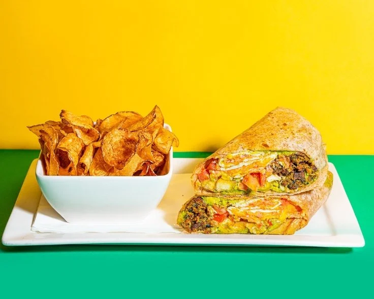 Cuban wrap with ham and roast pork served with crispy chips on a bright yellow-green plate at Empanada Mama NYC.