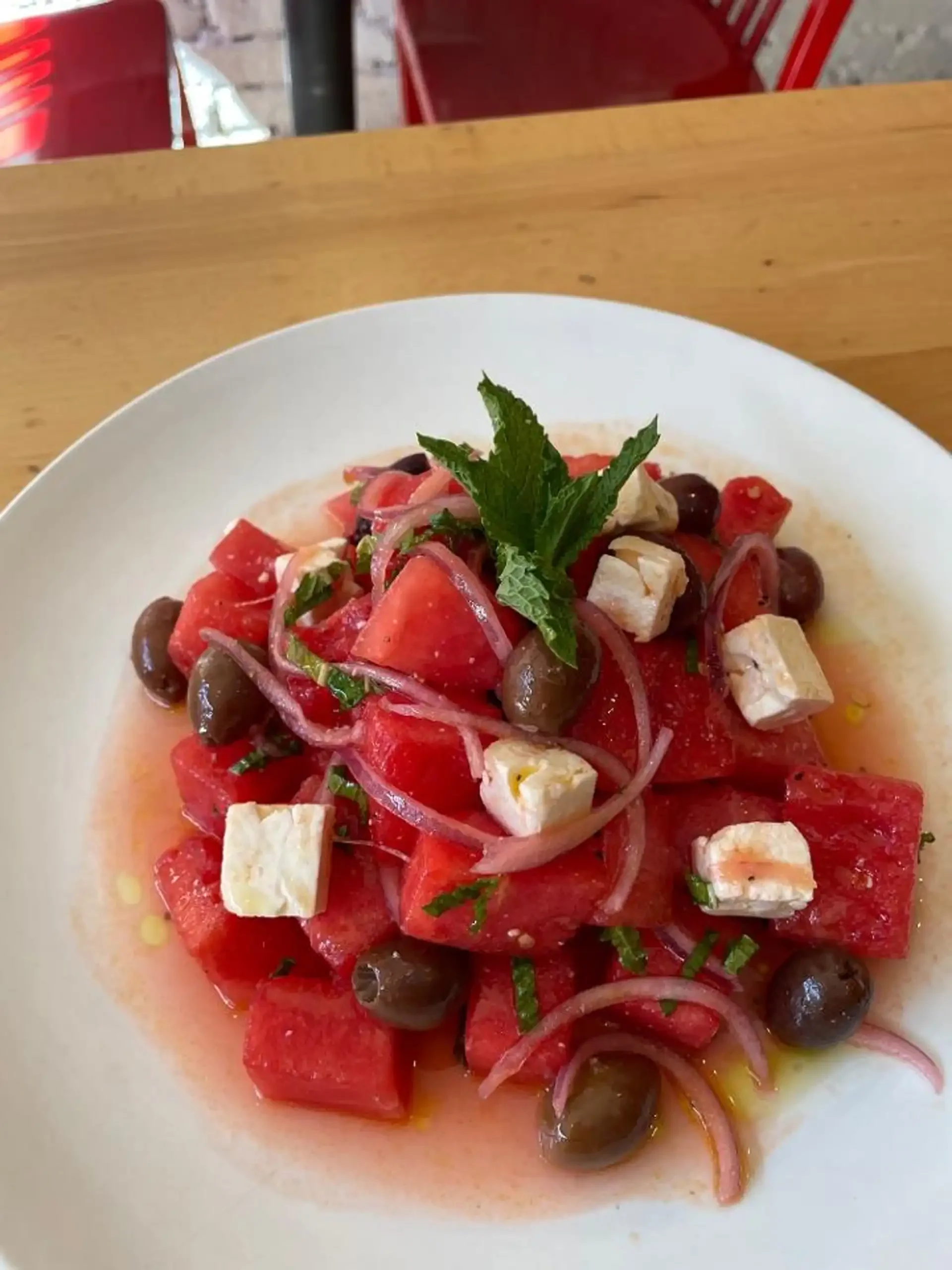 Fresh watermelon salad with feta, olives, and onions served at Empanada Mama — a refreshing complement to sweet churritos and empanadas.