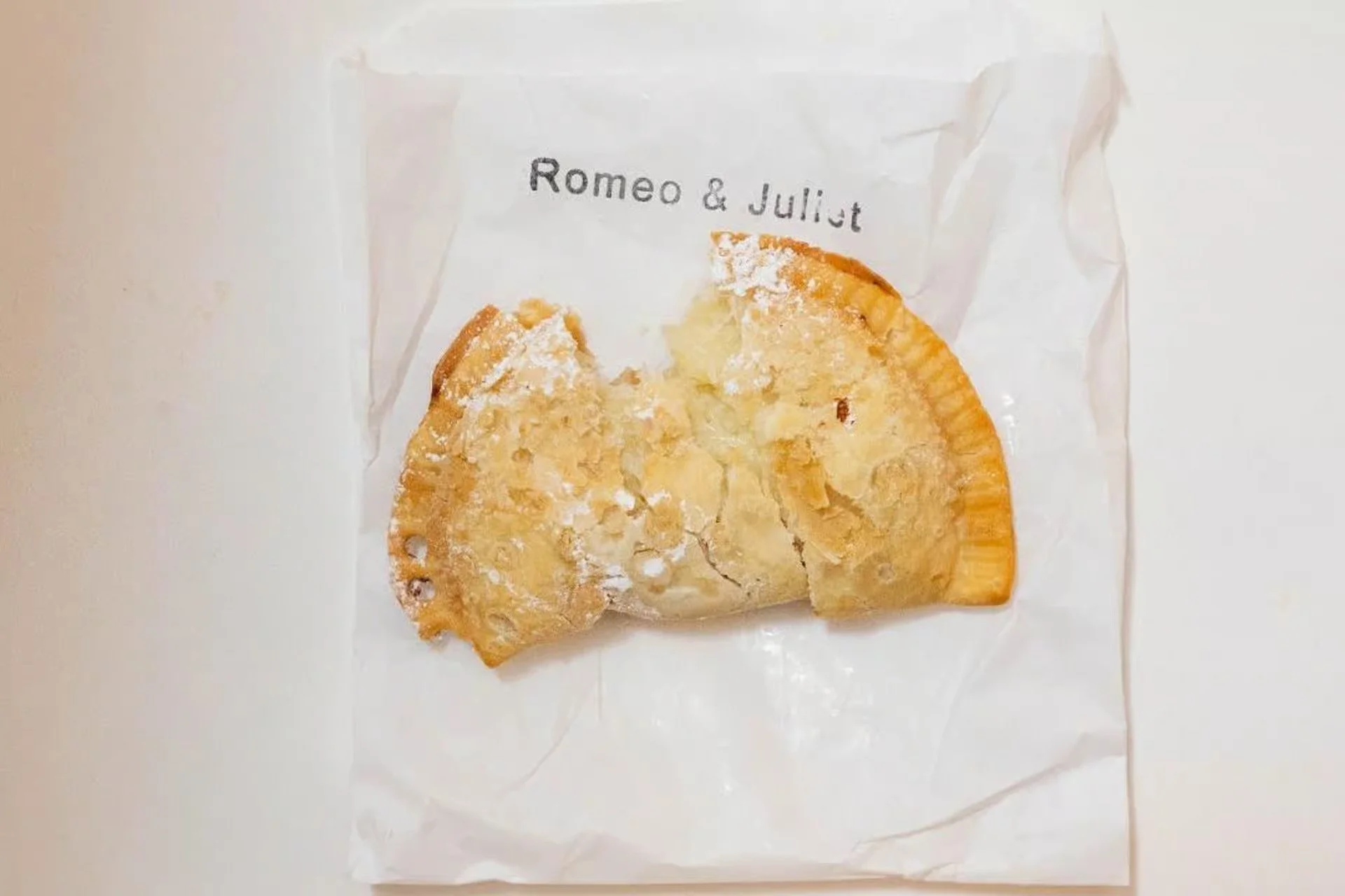 Powdered sugar–topped Romeo and Juliet dessert empanada served on white paper at Empanada Mama.