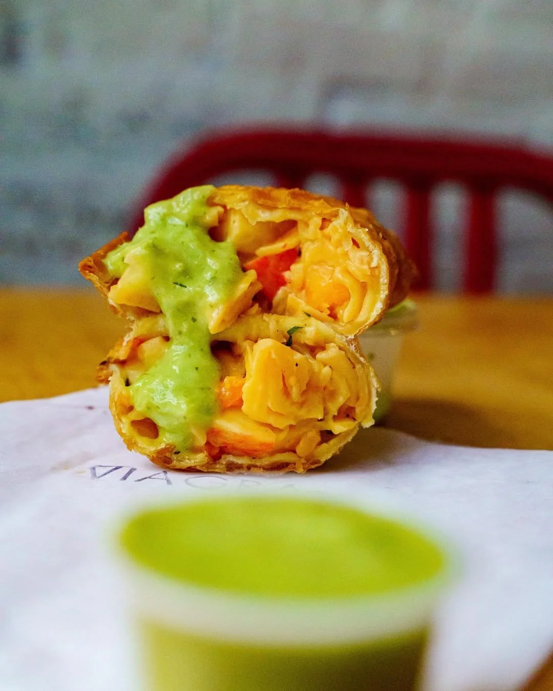 Crispy empanada filled with spiced filling, drizzled with green sauce.