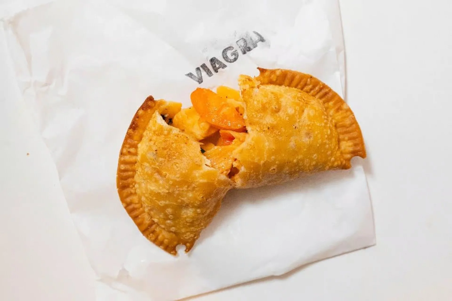 Close-up of a golden fried seafood empanada from Empanada Mama, cracked open to reveal its steamy, savory filling.