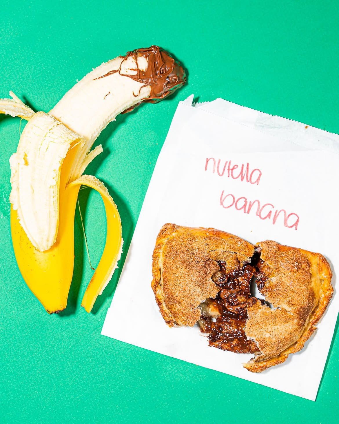 Chocolate-filled dessert empanada from Empanada Mama broken open beside a peeled banana, showcasing its warm, rich filling.