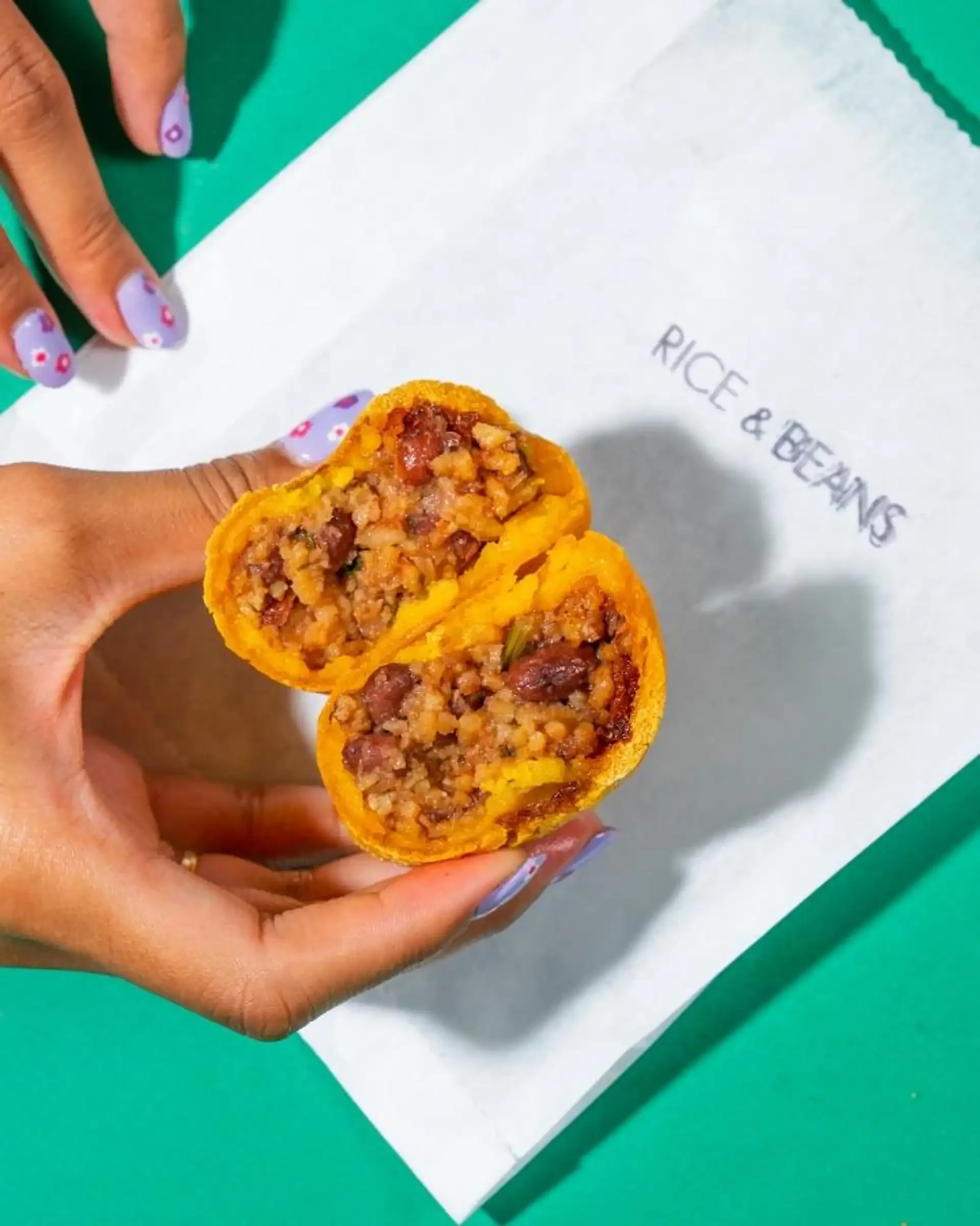 Rice and beans empanada split open in hand, showing a hearty filling from Empanada Mama on white paper.