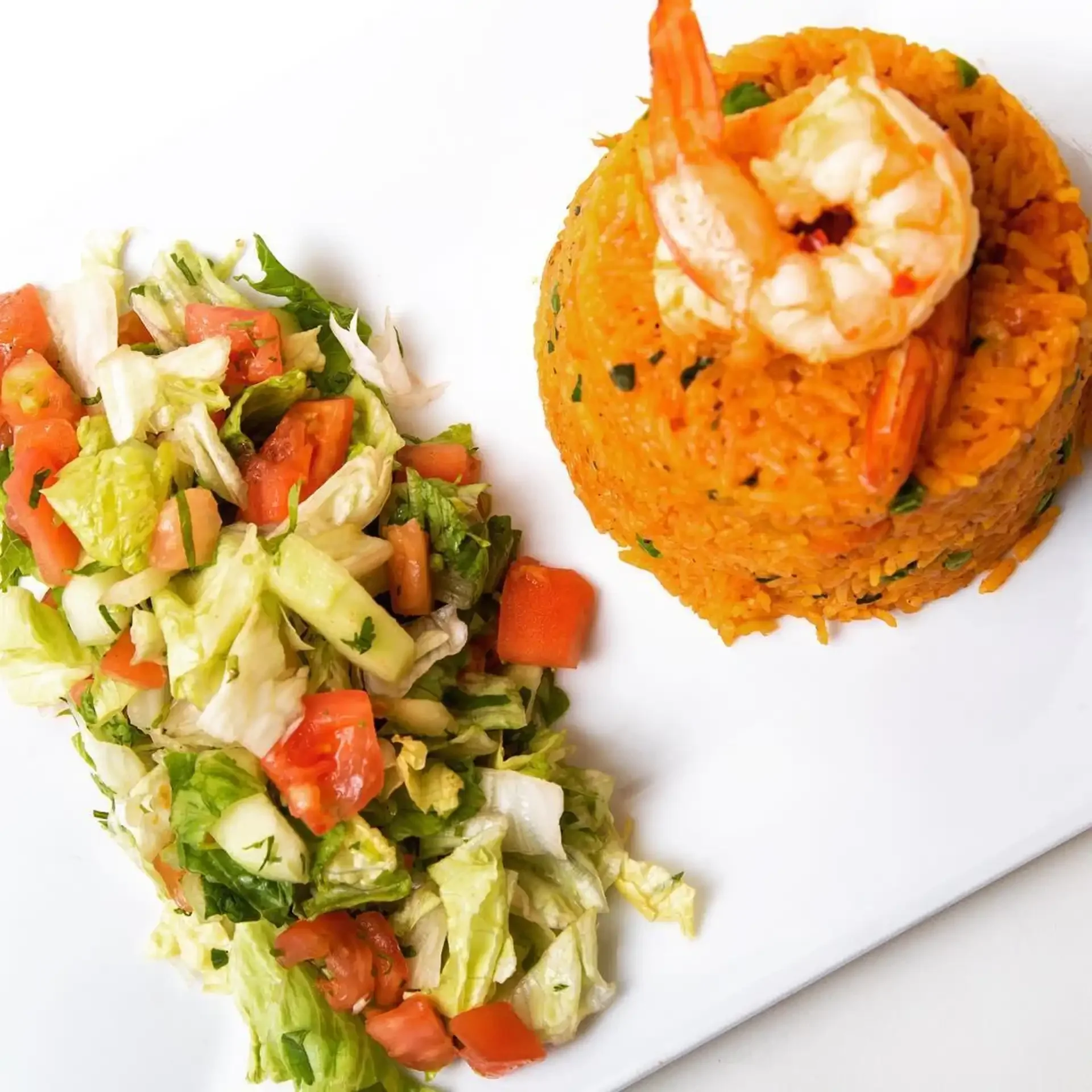 Shrimp rice platter with fresh chopped salad served on a white plate from Empanada Mama.