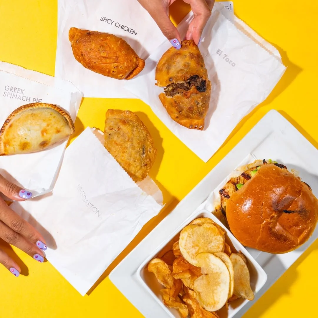 Assorted snacks including a burger, empanadas, and chips in takeout bags.