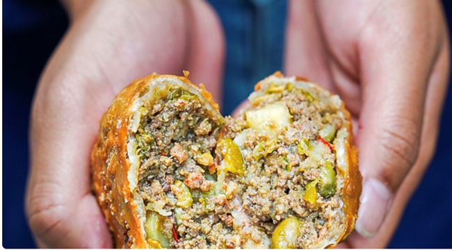 A hand holding a golden-brown empanada cut in half, revealing a flavorful meat and vegetable filling.