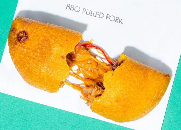 Empanada Mama BBQ pulled pork empanada pulled apart to reveal melted cheese and savory shredded pork filling on a teal background.