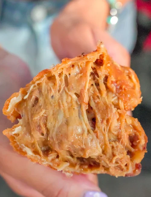 Close-up of an Empanada Mama empanada pulled apart, showing a warm, melty cheese-filled interior and flaky crust.