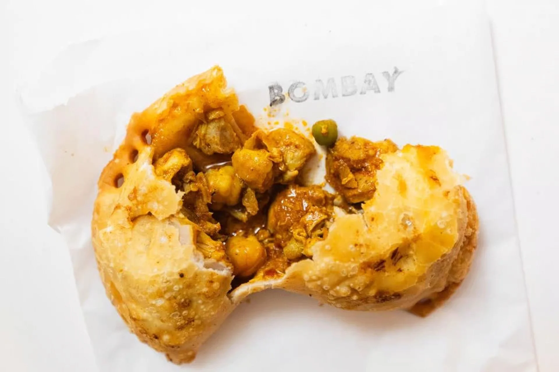 Bombay-style empanada broken open to reveal a spiced filling, served on white paper from Empanada Mama.