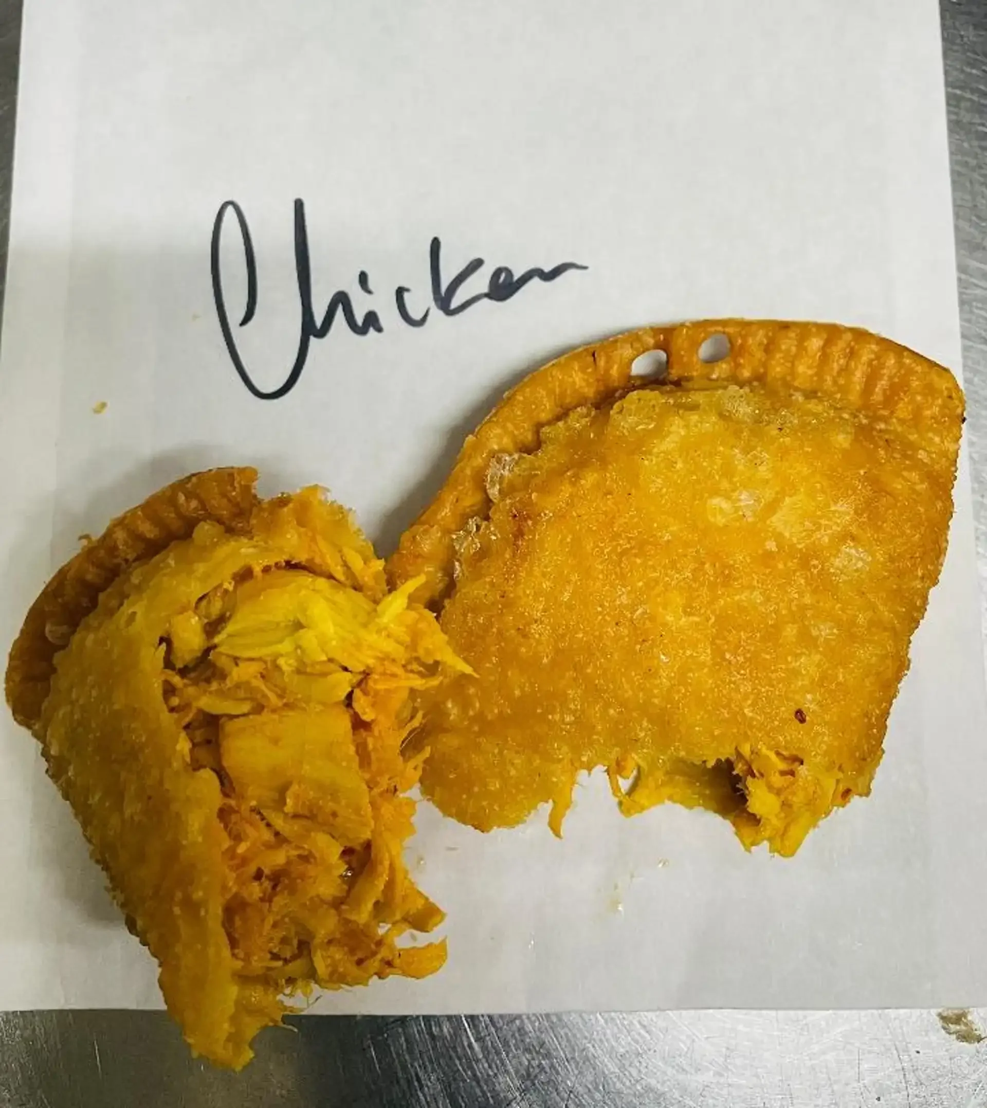 Chicken empanada from Empanada Mama, cut open to reveal shredded filling on branded paper.