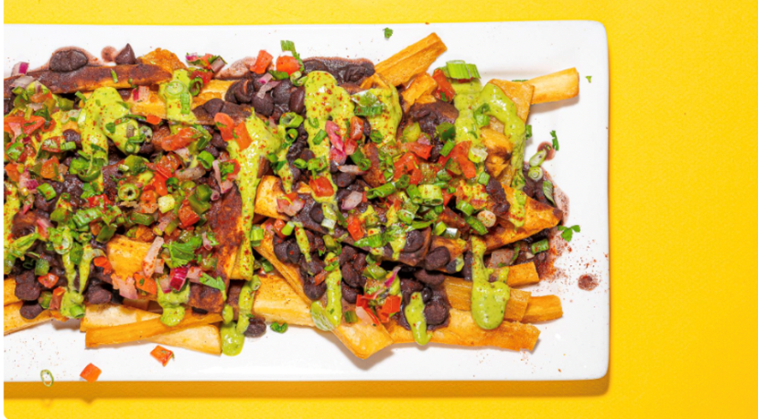 A plate of crispy fries topped with black beans, salsa, and a creamy green sauce.