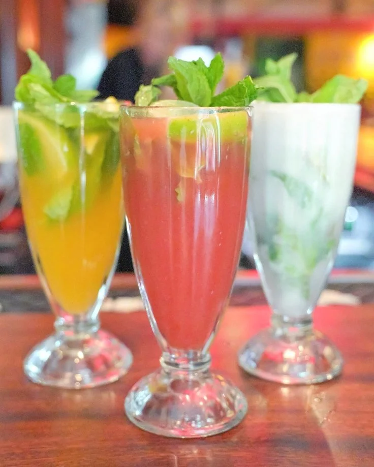 Yellow passion fruit, red strawberry, and white coconut mocktails garnished with mint at Empanada Mama NYC.