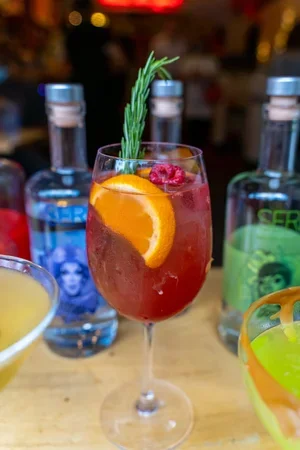 Festive red cocktail from Empanada Mama garnished with orange slices, cranberries, and rosemary, served in a stemmed glass.