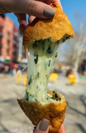 Empanada Mama spinach-and-cheese empanada, pulled apart, with melted cheese outdoors.