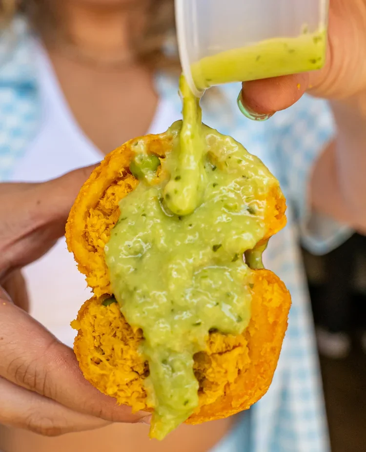 Close-up of chicken empanada topped with fresh green sauce being poured at Empanada Mama NYC.