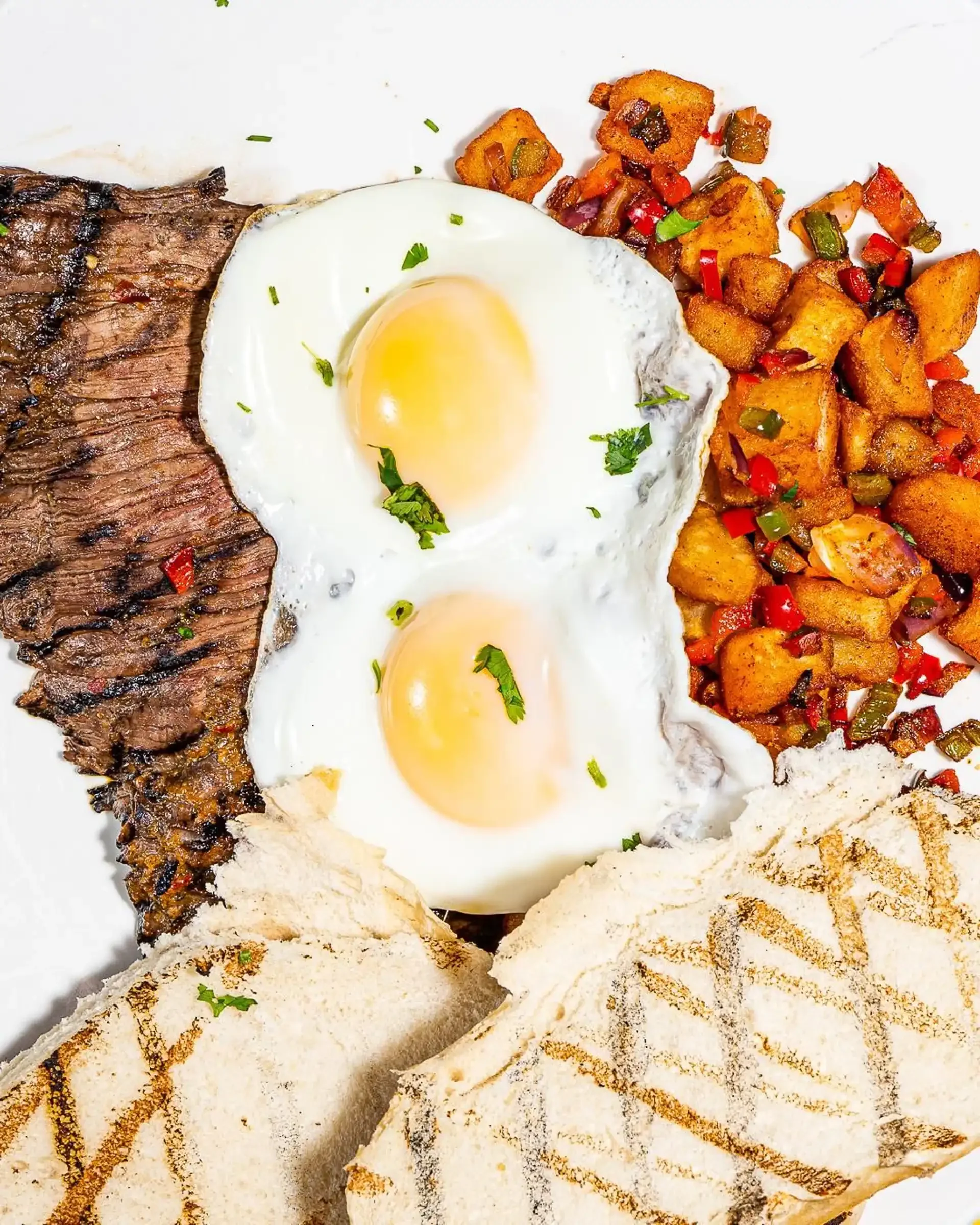 Colombian breakfast plate with steak, eggs, roasted potatoes, and bread served at Empanada Mama NYC.