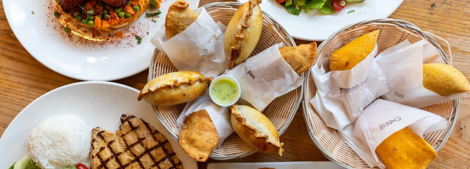 An assortment of empanadas and other food items available at Empanada Mama, placed on a wooden table.