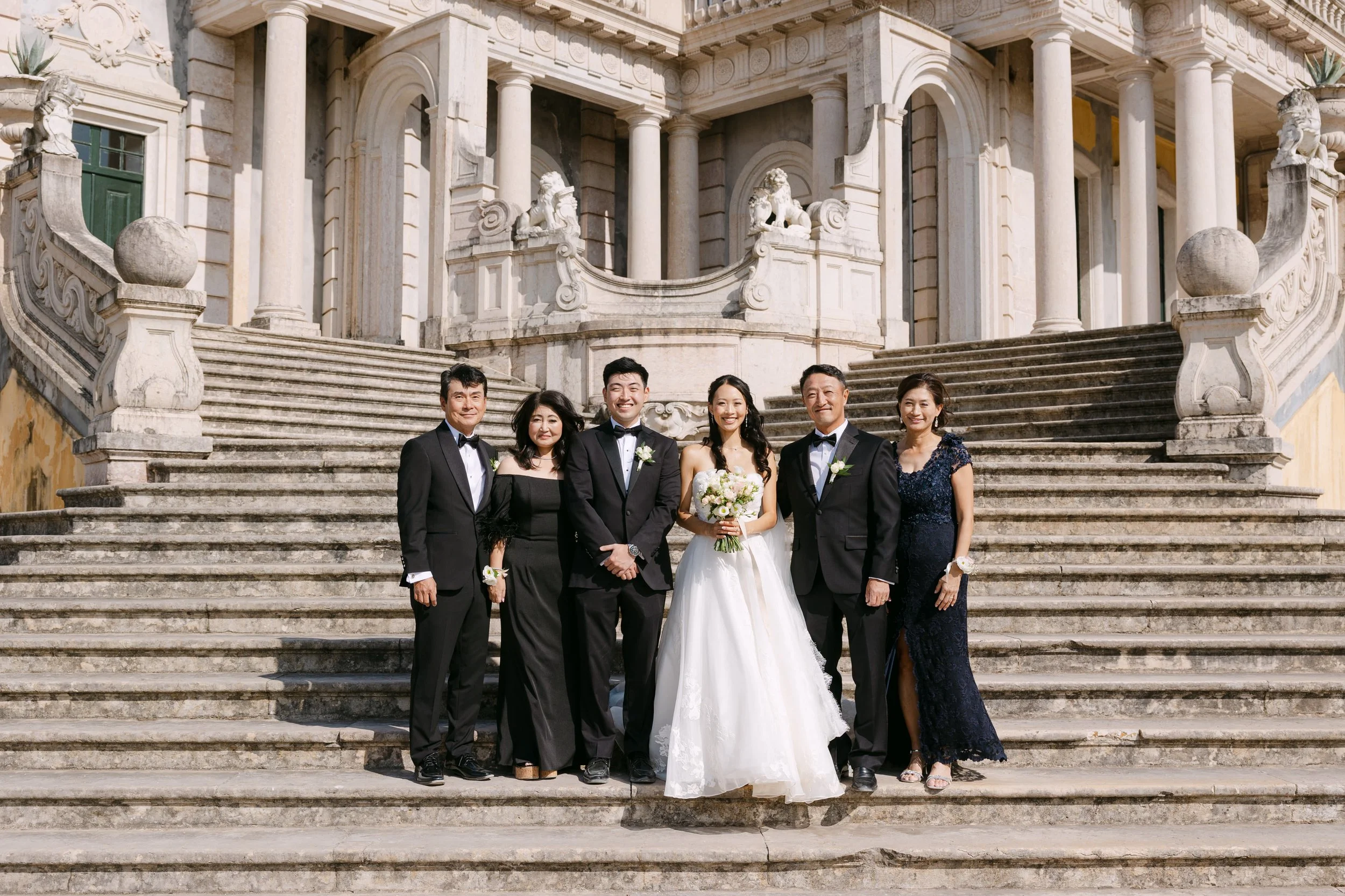 Bride and groom surrounded by family for a formal group portrait on the historic staircase at Palácio Nacional de Queluz.