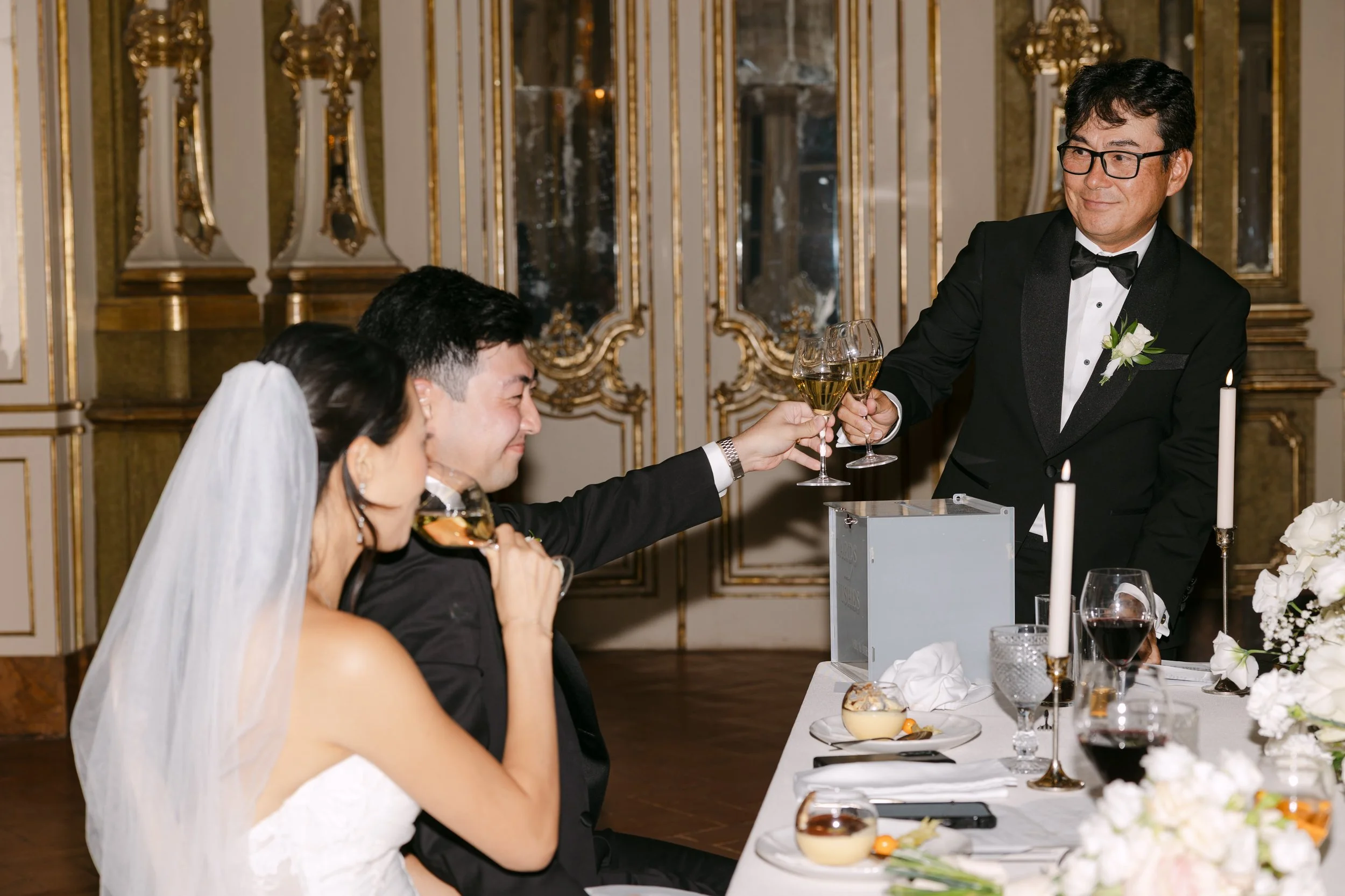 Wedding guest raising a glass during the reception as the newlyweds smile from their table inside Palácio Nacional de Queluz.
