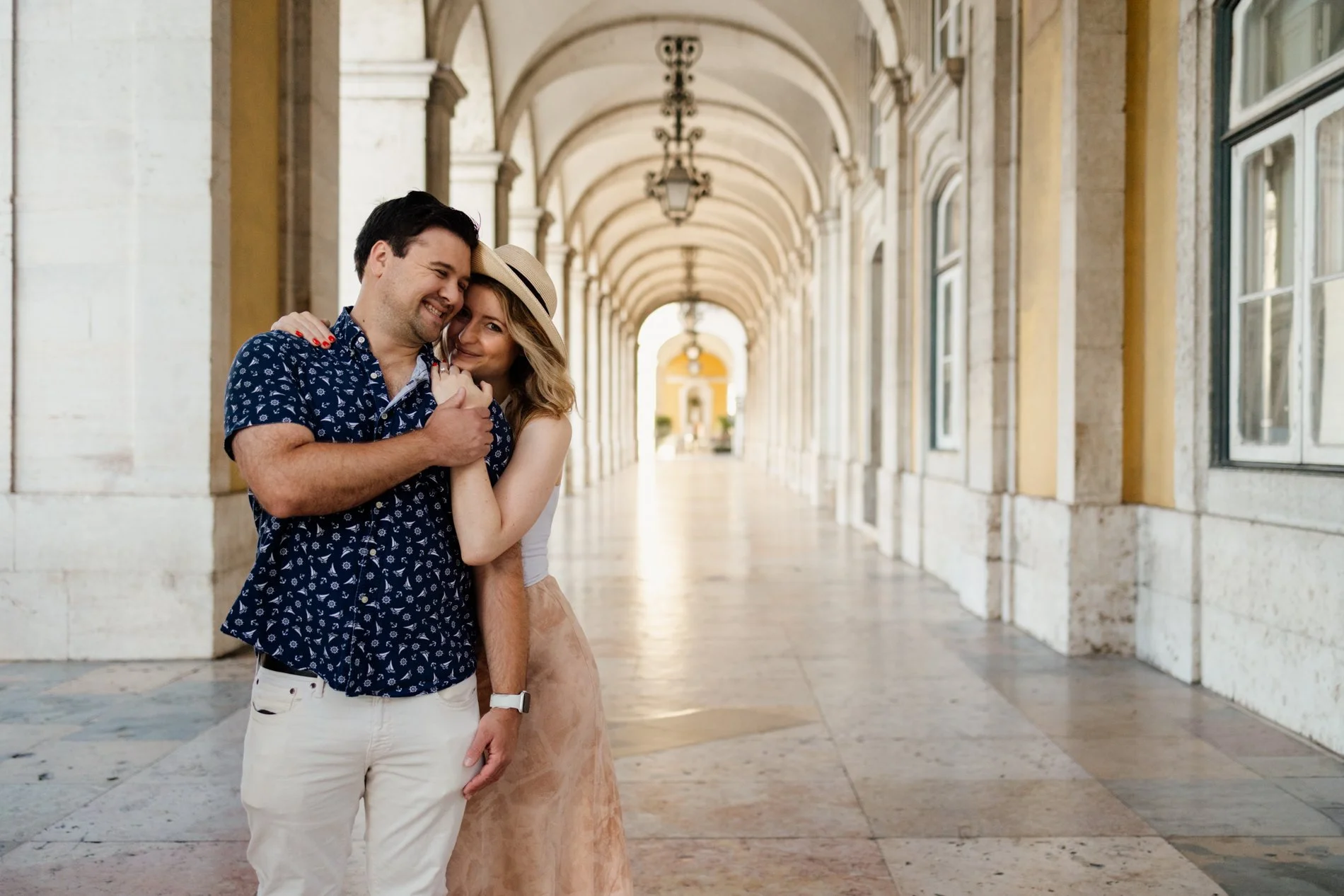 Couple embracing beneath the historic arches of Praça do Comércio during an engagement photoshoot in Lisbon, Portugal.