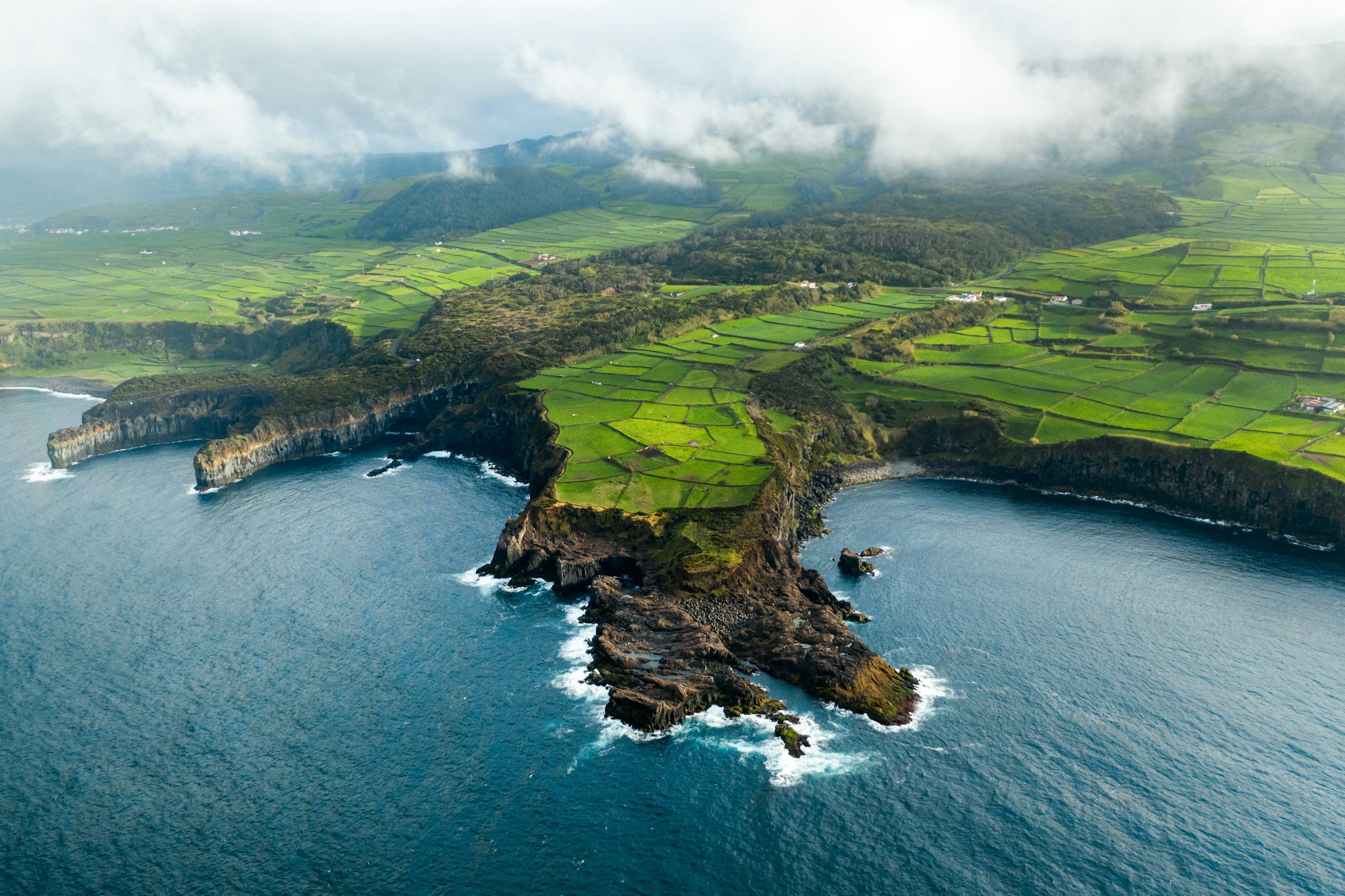 Aerial view of the Azores coastline with green fields and volcanic cliffs.