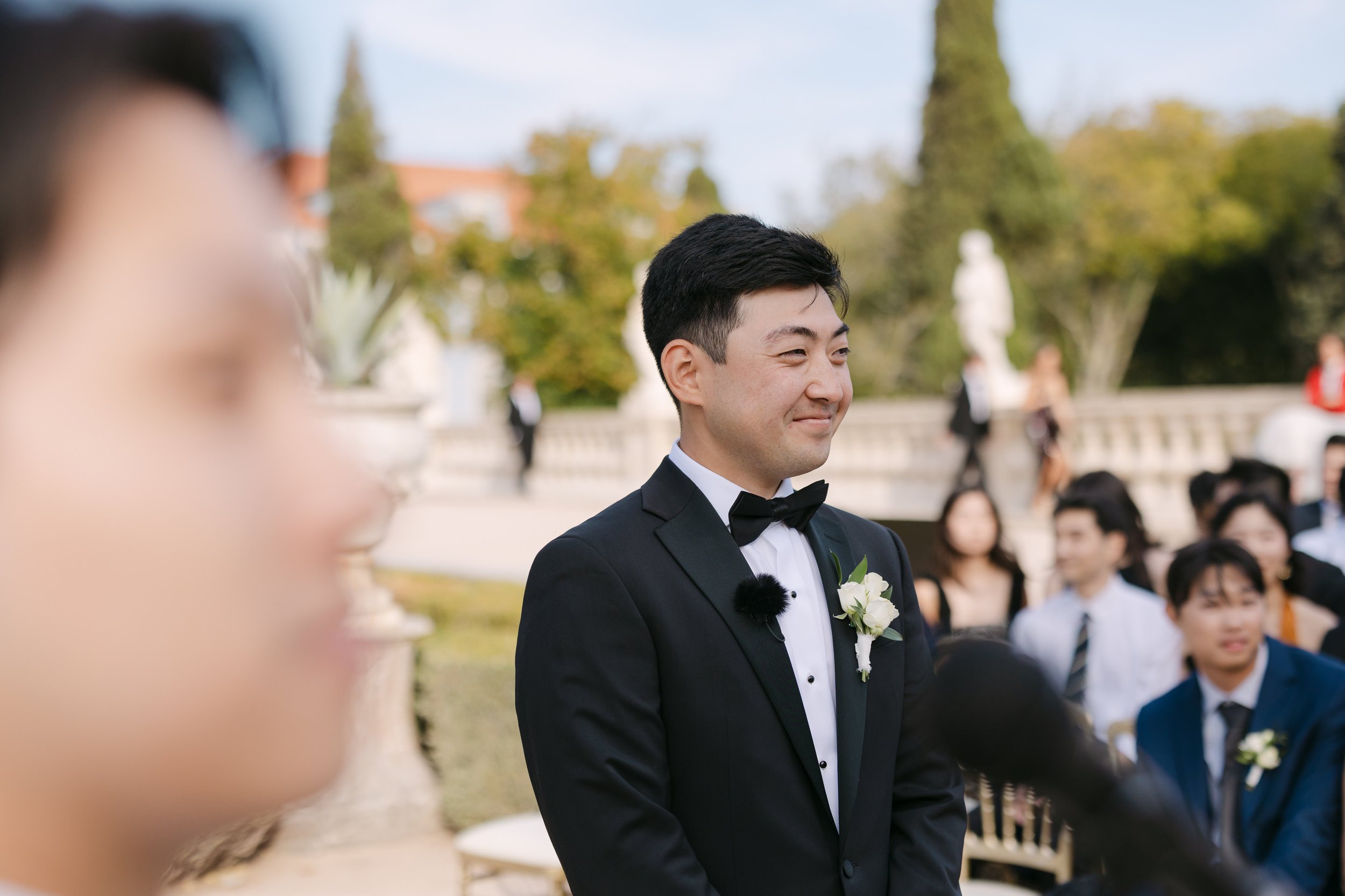 Groom smiling as he waits for the bride during their outdoor wedding ceremony in the gardens of Palácio Nacional de Queluz.
