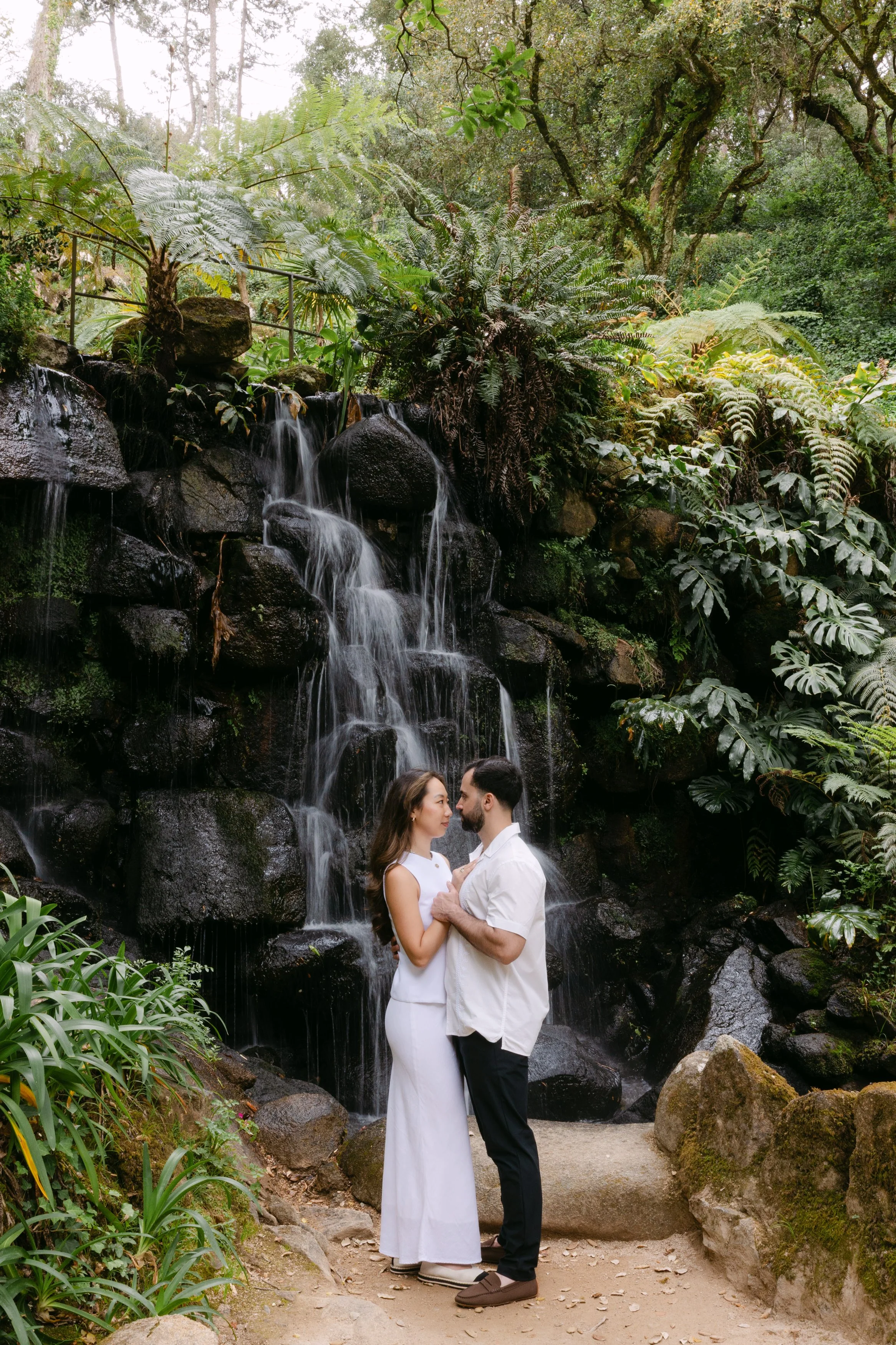 Engaged couple standing beside a waterfall during romantic photoshoot at Monserrate in Sintra.