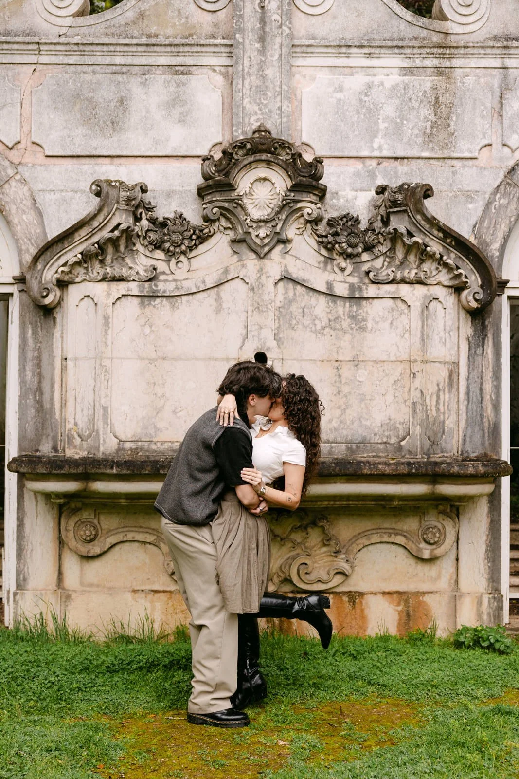 Newly engaged couple embracing in front of a historic fountain at Tapada das Necessidades in Lisbon