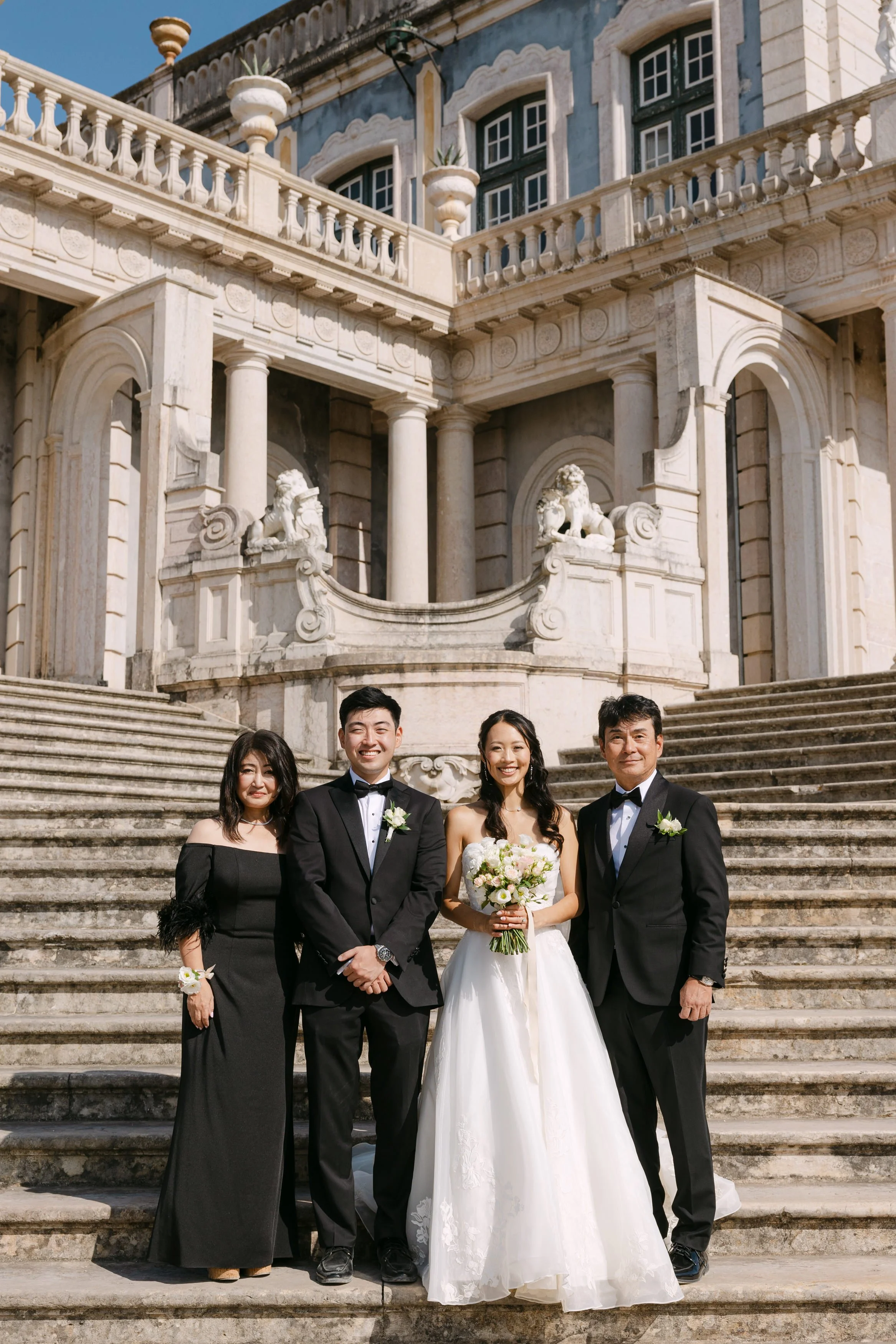 Bride and groom smiling with the bride’s family during a wedding portrait on the grand staircase of Palácio Nacional de Queluz.