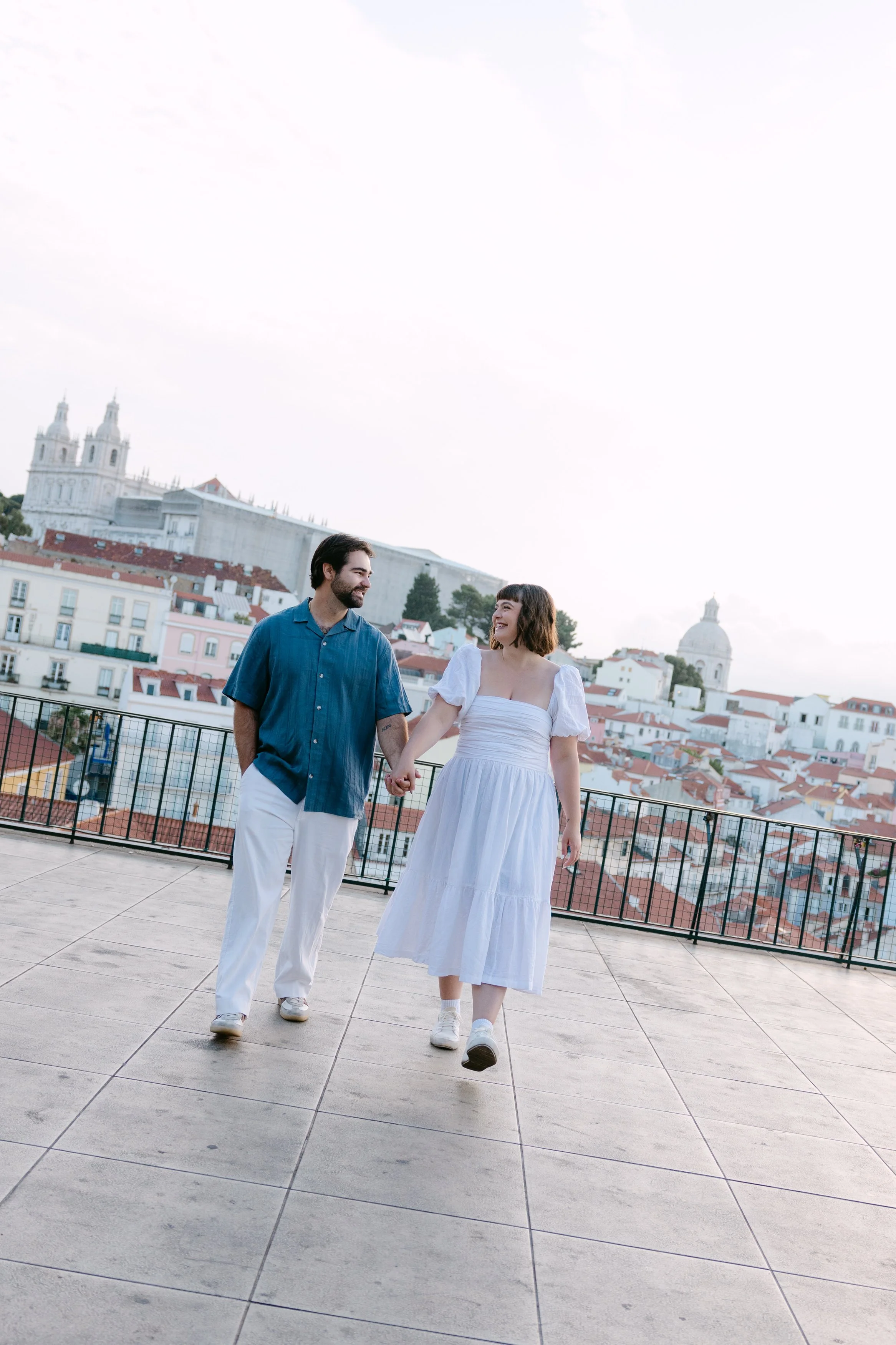 Newly engaged couple laughing and walking together at Miradouro das Portas do Sol in Lisbon.