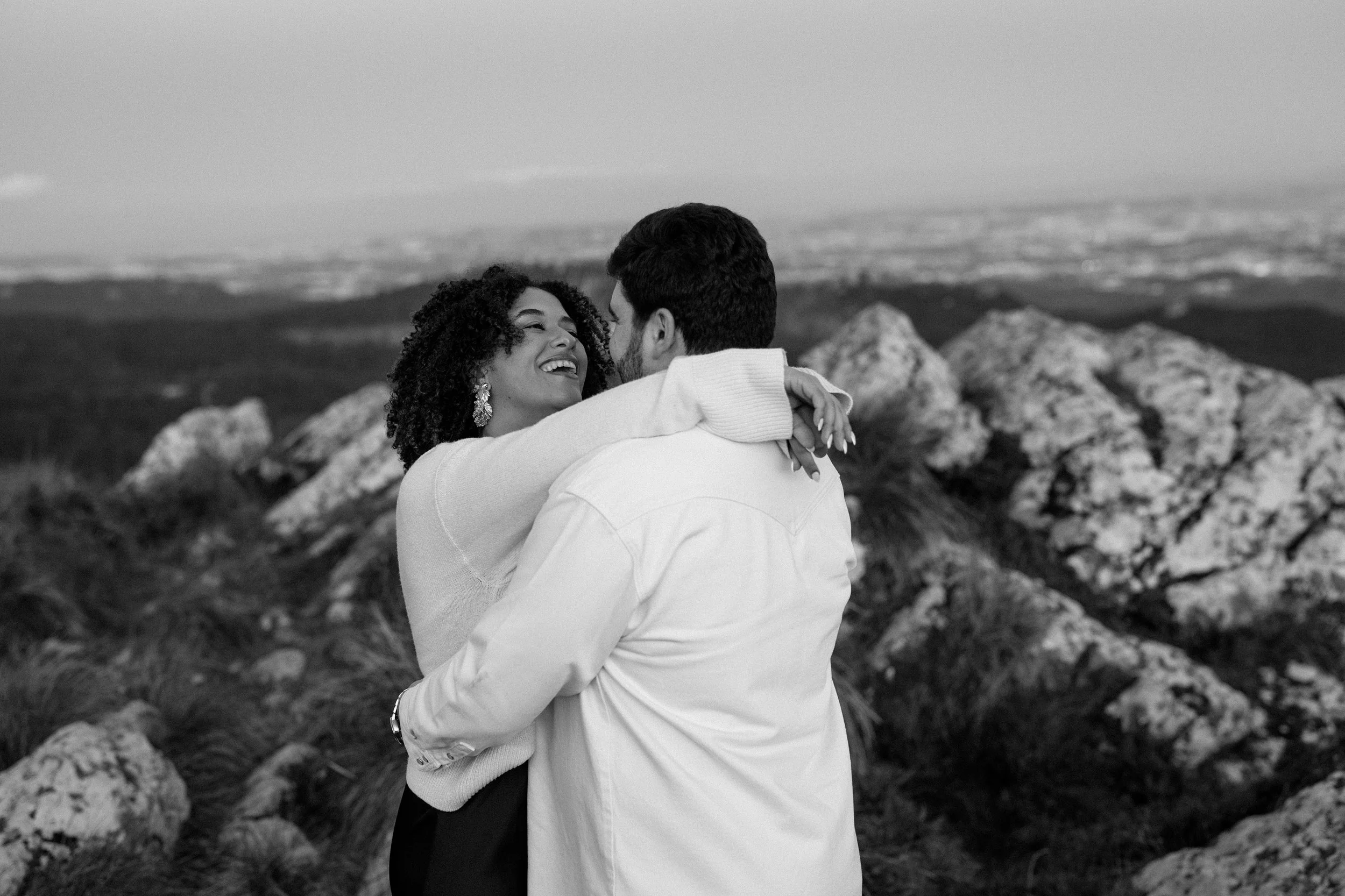 Black and white engagement portrait of couple embracing on rocky landscape in Sintra