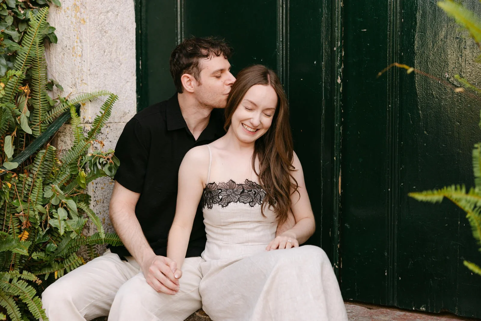 Newly engaged couple sitting together as he kisses her forehead during their engagement photos at Quinta de Sant’Ana in Portugal.