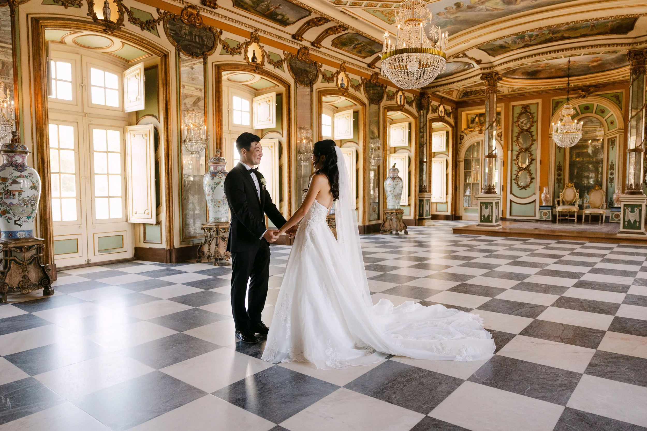 Bride and groom holding hands and smiling at each other after their first look inside an ornate room at Palácio Nacional de Queluz.