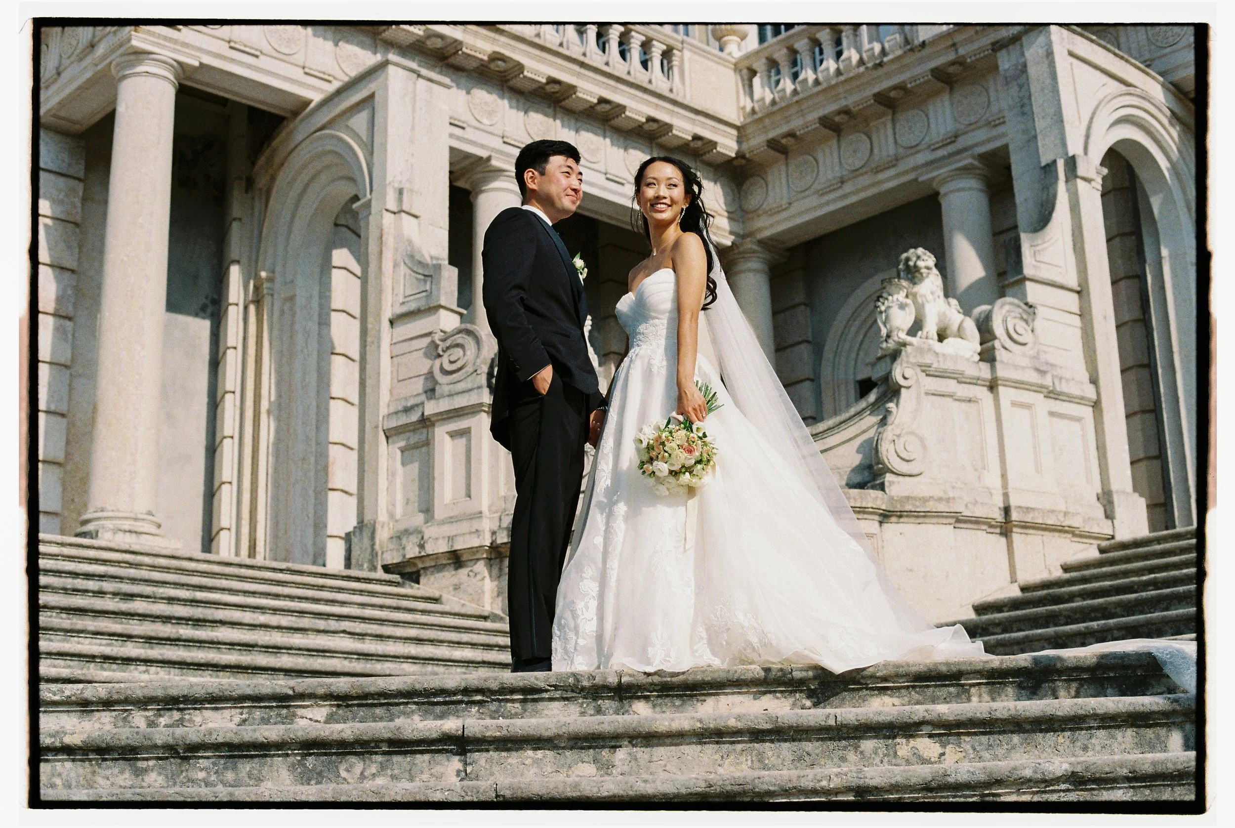 Bride and groom photographed on film on the grand palace steps during their wedding at Palácio Nacional de Queluz, Portugal.