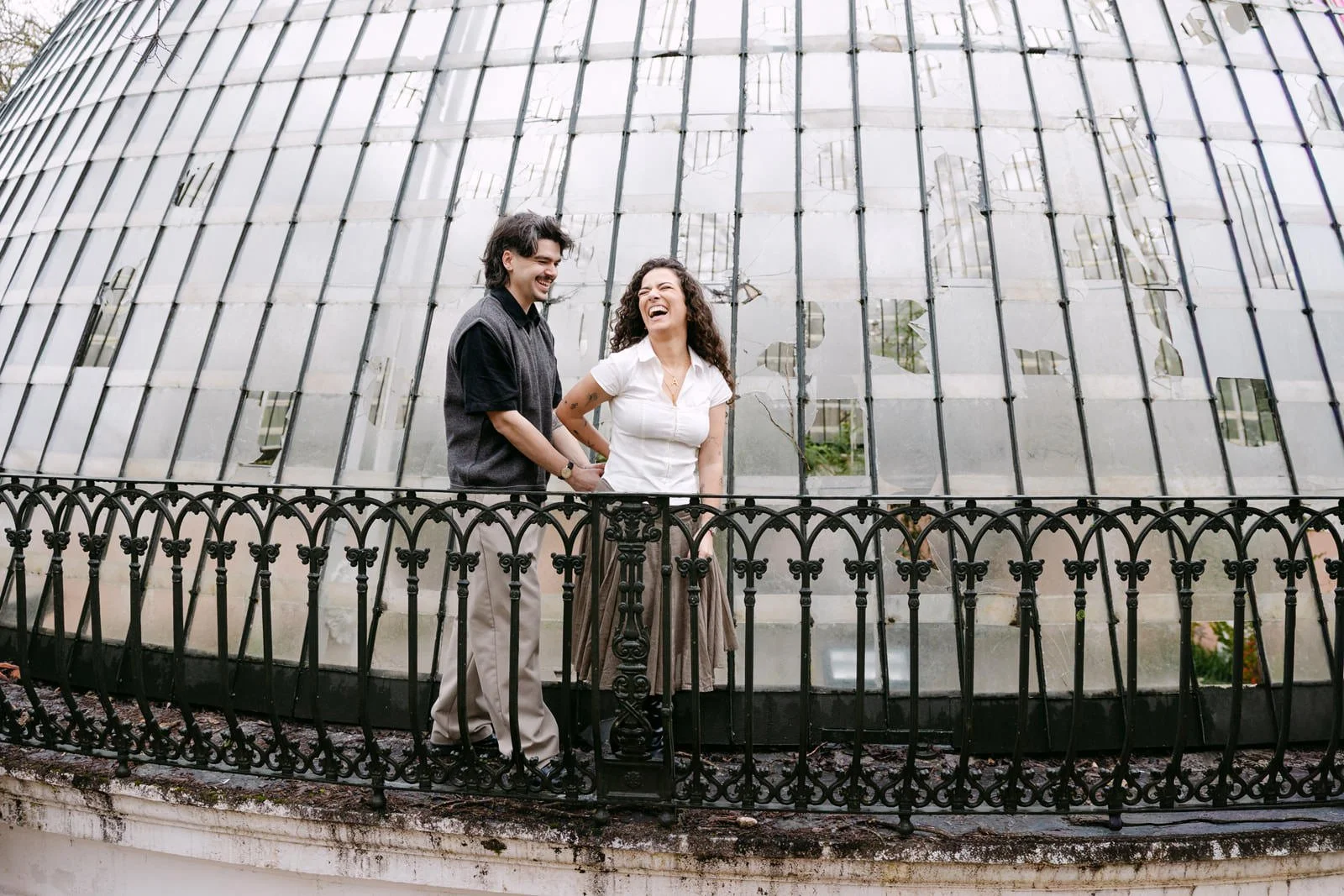 Engaged couple laughing in front of the historic greenhouse at Tapada das Necessidades in Lisbon