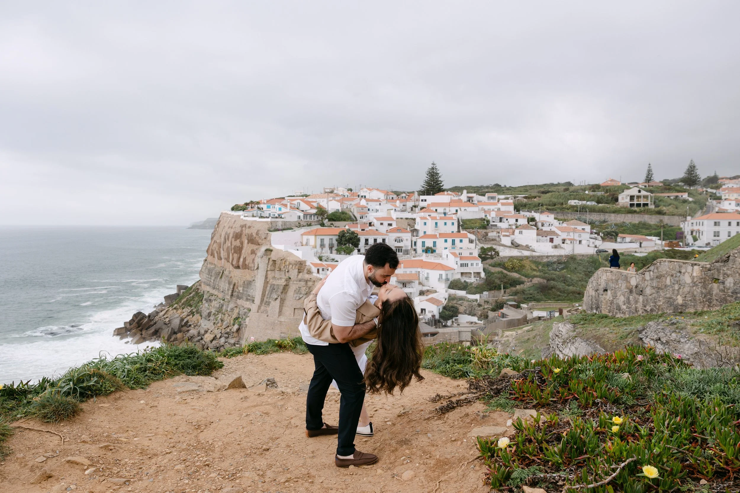 Couple kissing on the cliffs overlooking Azenhas do Mar during romantic Portugal photoshoot.