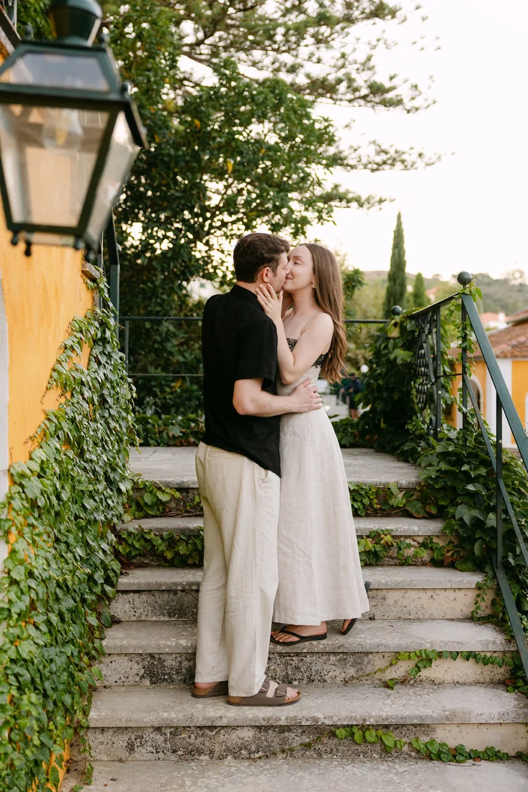 Newly engaged couple kissing on the stone steps surrounded by greenery at Quinta de Sant’Ana near Lisbon.