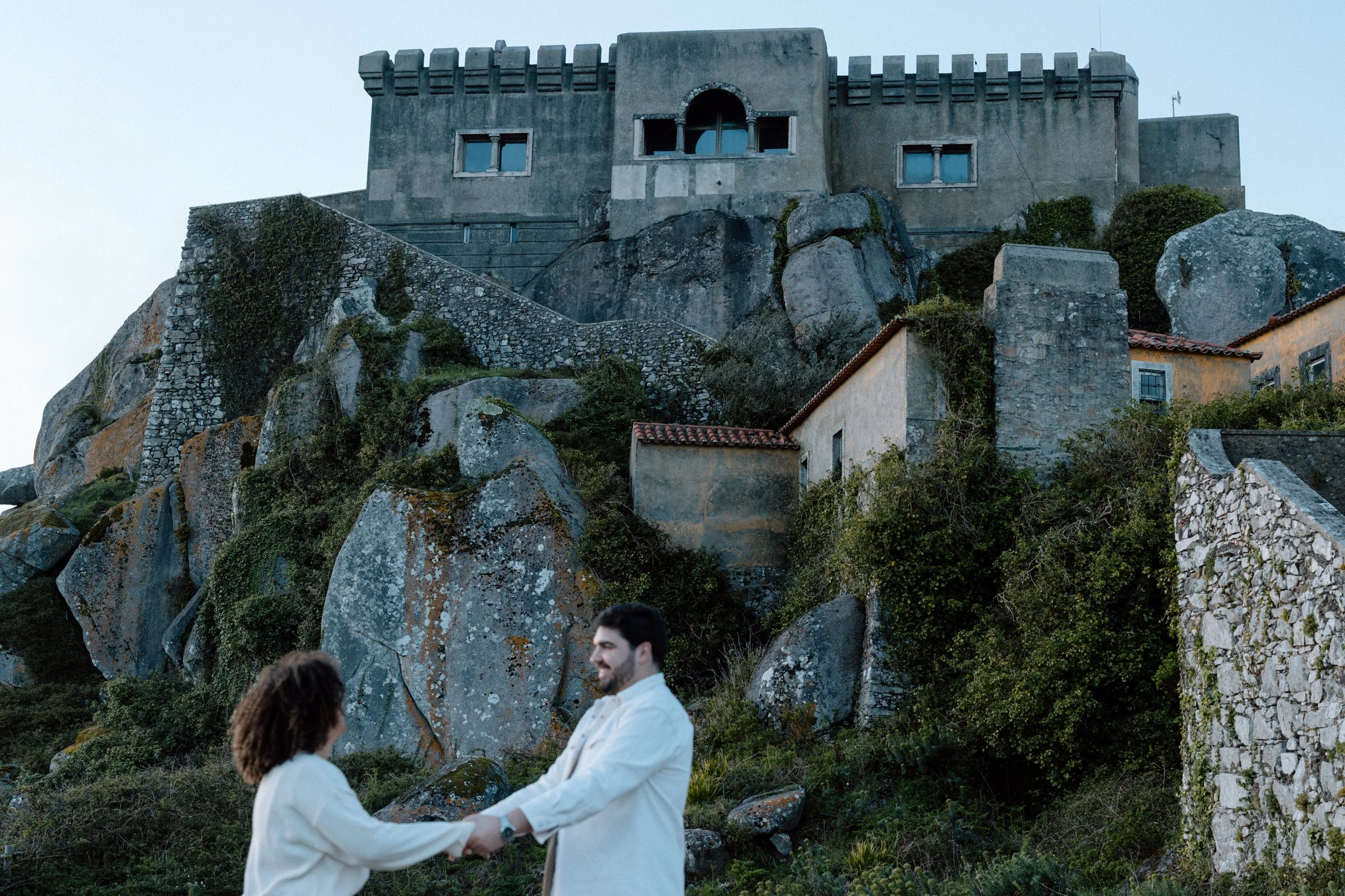 Engaged couple holding hands with Santuário da Peninha in the background