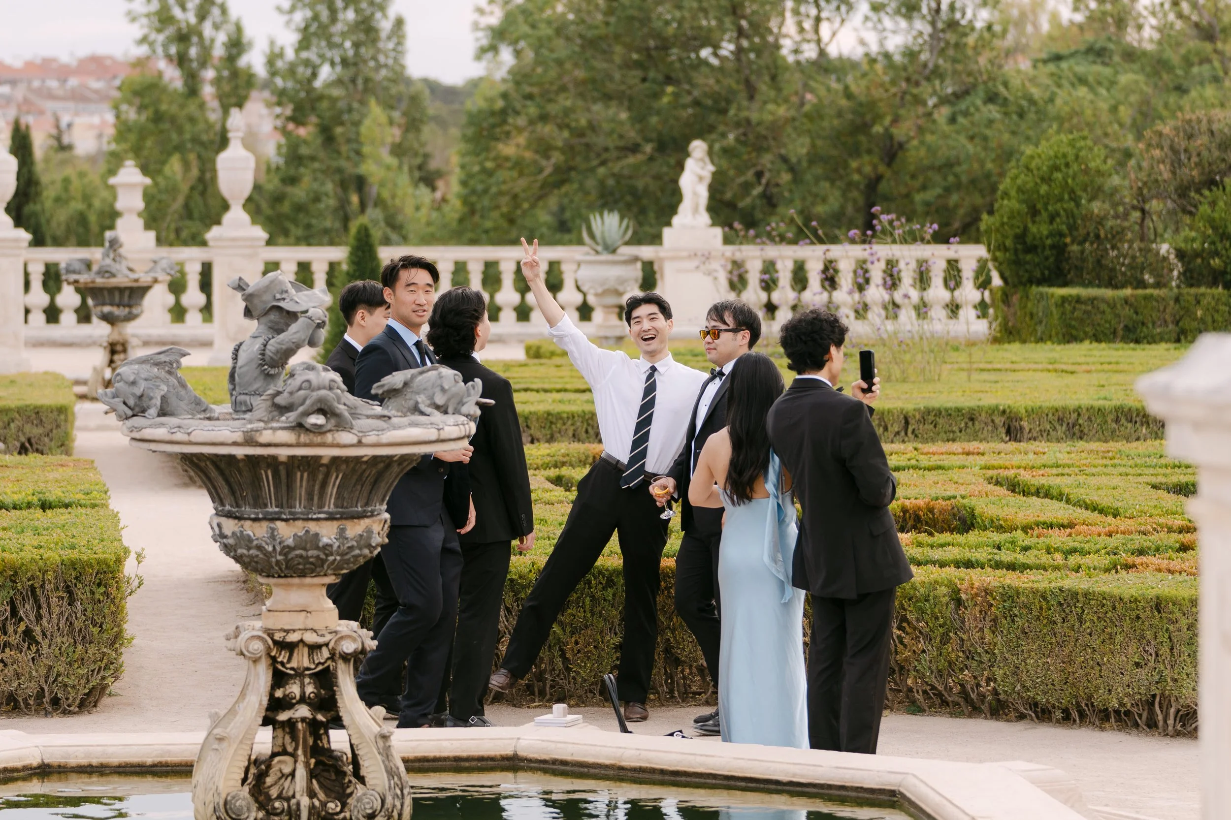 Wedding guests laughing and celebrating together during cocktail hour among the formal gardens of Palácio Nacional de Queluz.