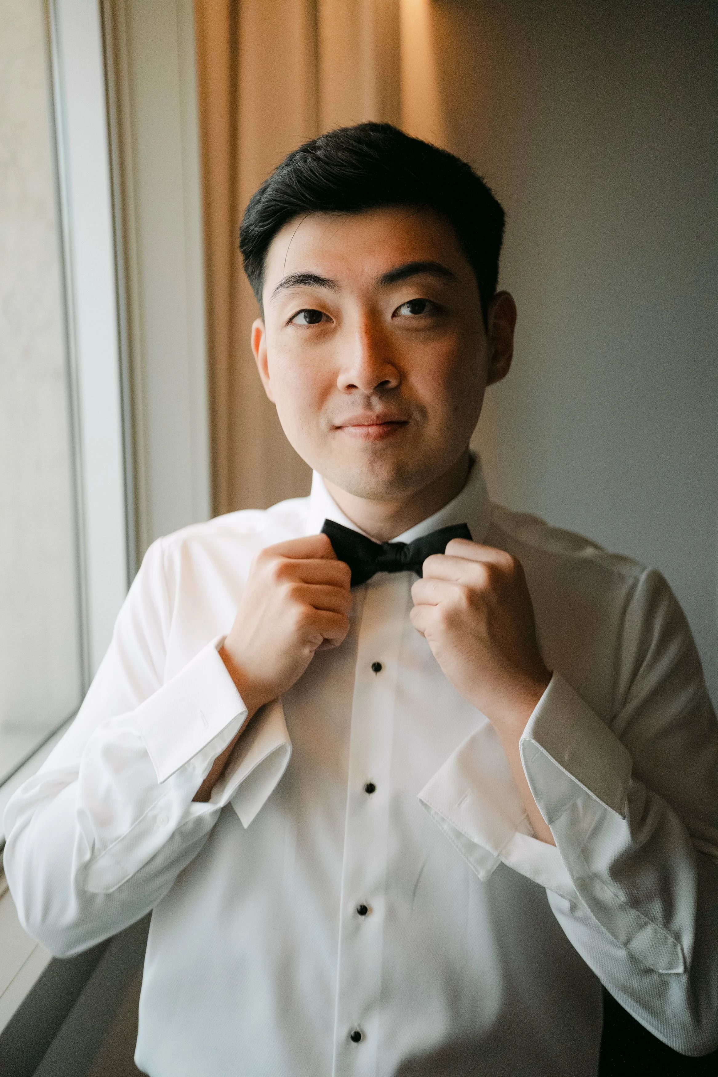 Groom adjusting his black bow tie while getting ready for his wedding at Palácio Nacional de Queluz.