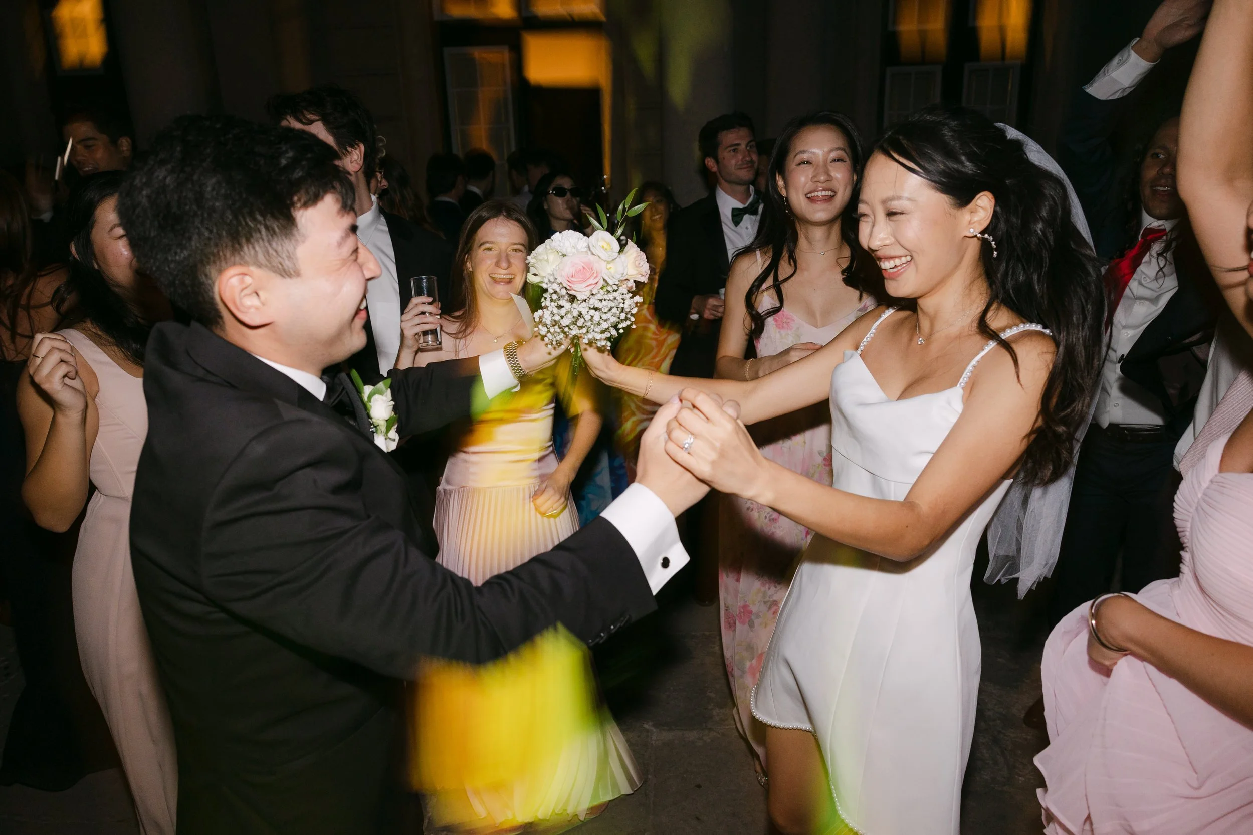 Bride and groom laughing and dancing together surrounded by friends during their nighttime wedding party at Palácio Nacional de Queluz.