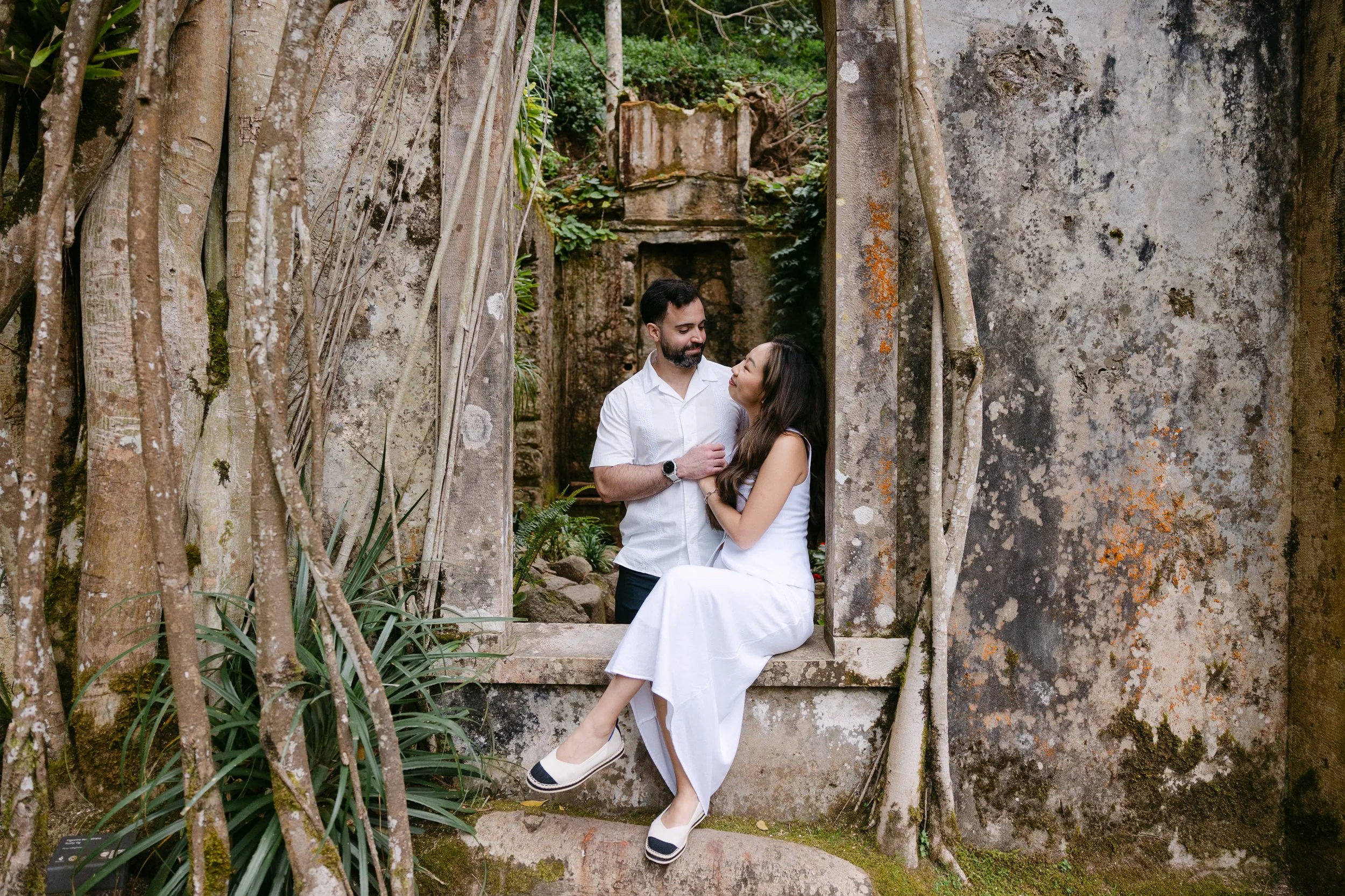 Couple enjoying a romantic engagement photoshoot in a hidden garden in Sintra, surrounded by historic stone ruins, ancient trees and lush greenery.