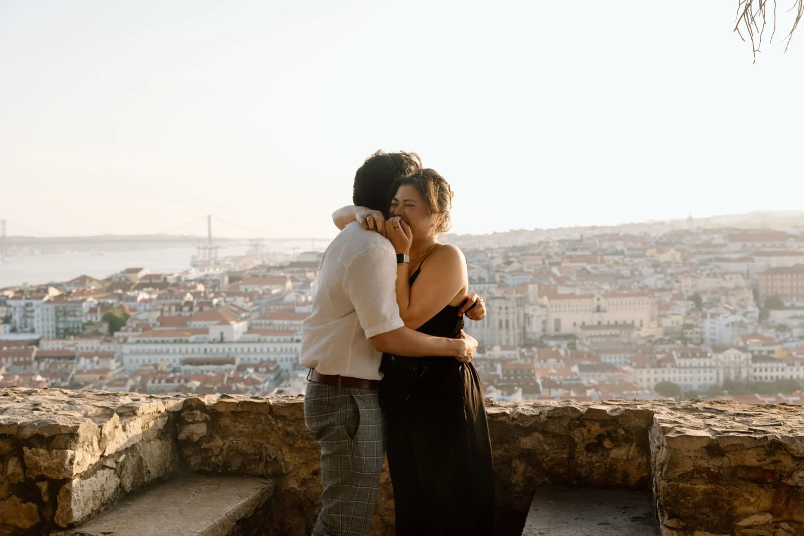 Just engaged couple embracing after a surprise proposal overlooking Lisbon at sunset.